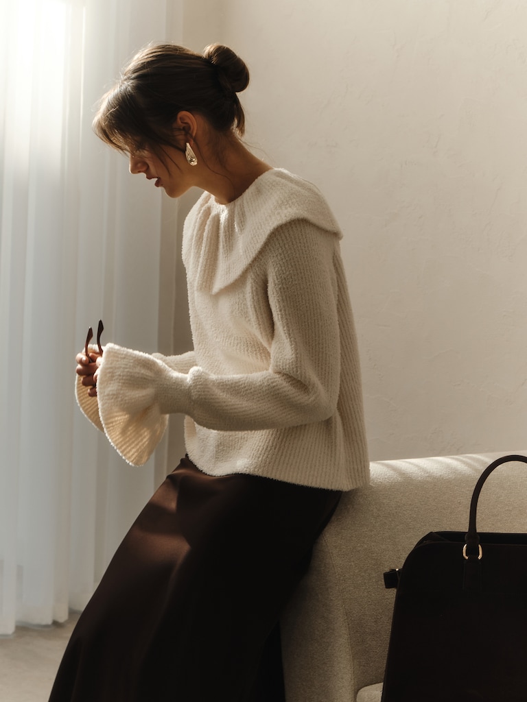 стильная женщина примеряет трикотажный пуловер перед зеркалом